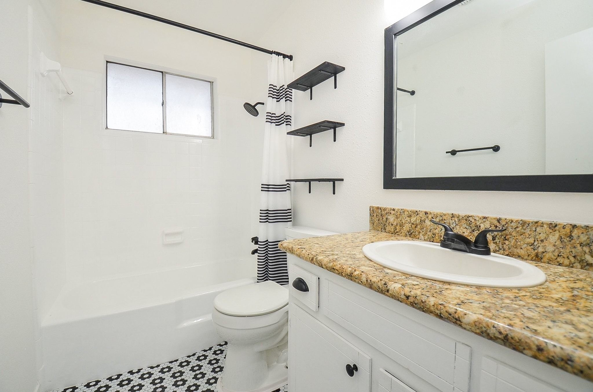 9014 Langfield Road Houston, TX 77040 - Photo 20 of 37 This stylishly updated full bathroom combines modern design accents with functional layout features. A warm granite vanity countertop pairs perfectly with dark matte hardware, high-contrast framed mirrors, and eye-catching black-and-white patterned tile flooring.