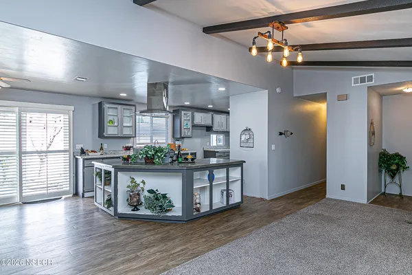 a view of an empty room and kitchen with wooden floor