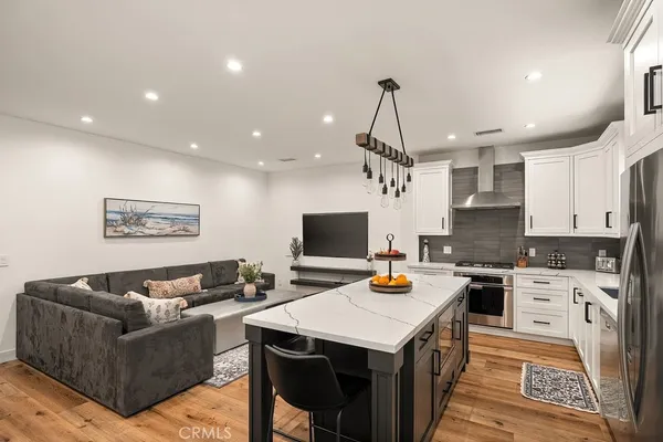 a view of a kitchen with kitchen island a stove a sink a refrigerator wooden floor dining table and chairs