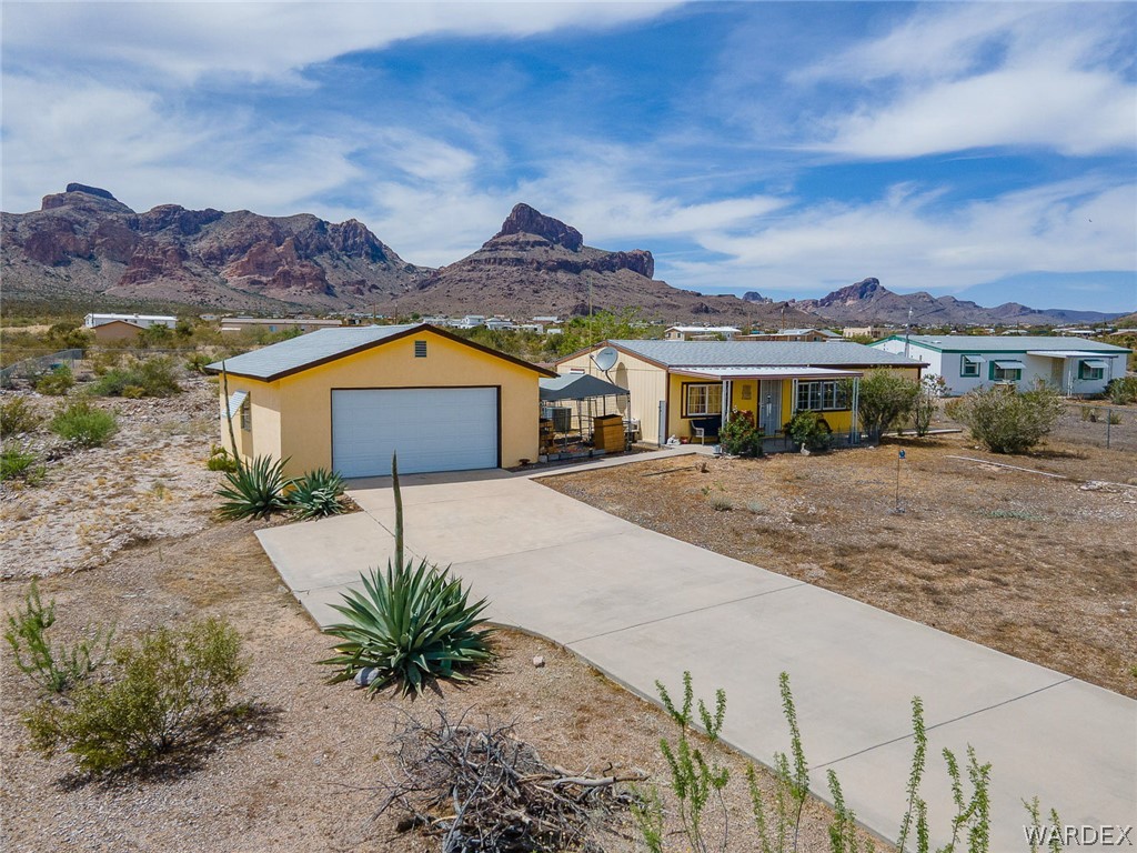 2465 Egar Road Golden Valley, AZ 86413 - Photo 77 of 98 The property features a primary dwelling and an additional structure, both with yellow exteriors and light-colored roofs, set against a backdrop of mountains