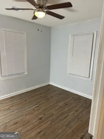a view of an empty room with wooden floor and fan