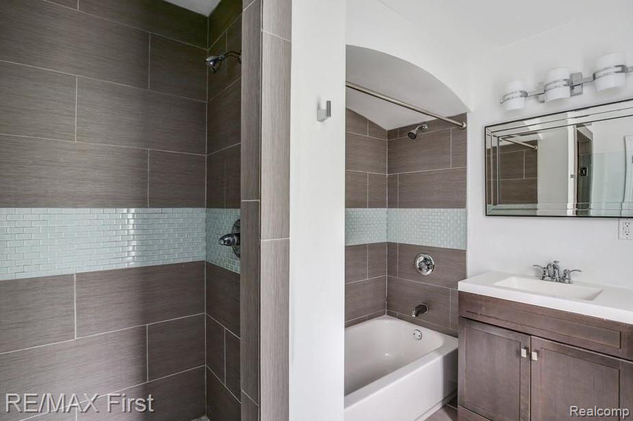 1349 Devonshire Road Grosse Pointe, MI 48230 - Photo 14 of 26 Bathroom featuring a tiled shower and tub combination with a mosaic accent band, a single vanity with a white countertop and undermount sink, a framed mirror, and a three-light vanity fixture