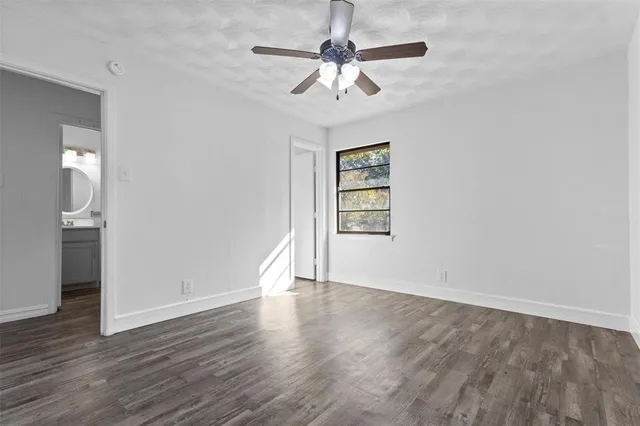 an empty room with wooden floor chandelier fan and windows