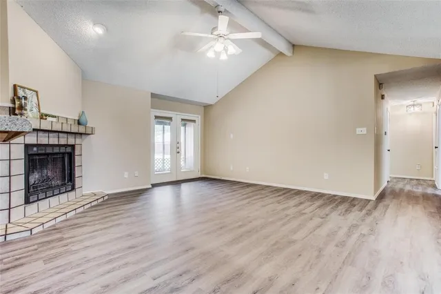 an empty room with wooden floor a ceiling fan a fireplace and windows