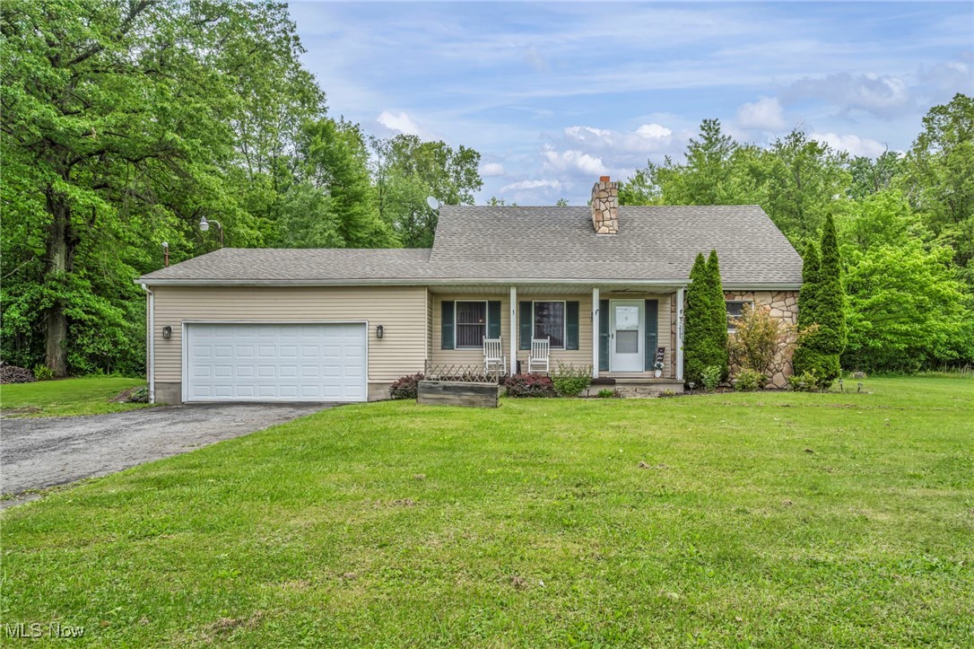 View of front of home with an attached garage, a chimney, a porch, asphalt driveway, and a front yard