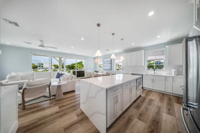 a large white kitchen with a large window a island and stainless steel appliances