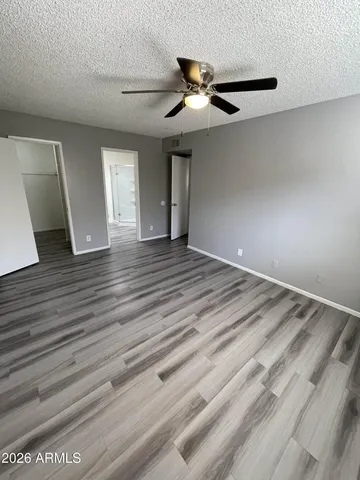 a view of an empty room with wooden floor and a ceiling fan