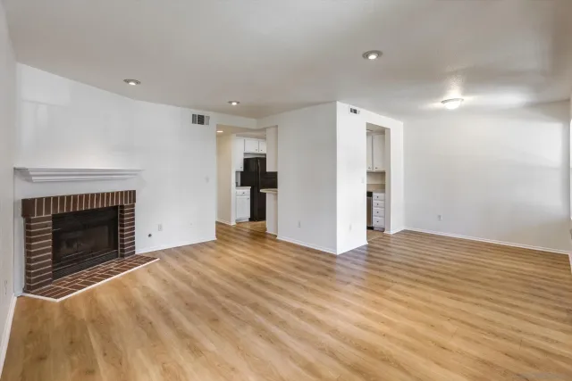 a view of an empty room with wooden floor fireplace and a window