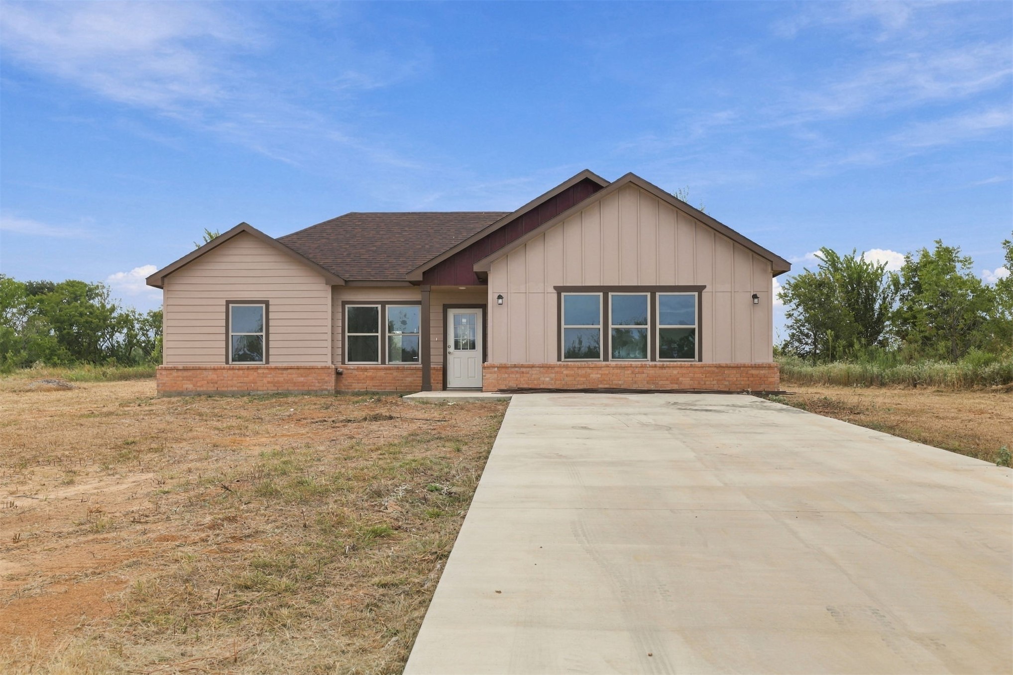 21 Redbird Lane Colbert, OK 74733 - Photo 23 of 27 Single-story residence featuring a concrete driveway, brick foundation, tan siding, brown roof, and dark-framed windows