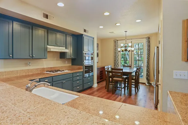 a kitchen with stainless steel appliances granite countertop a stove top oven a sink a dining table and chairs with wooden floor