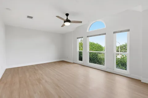 an empty room with wooden floor ceiling fan and window