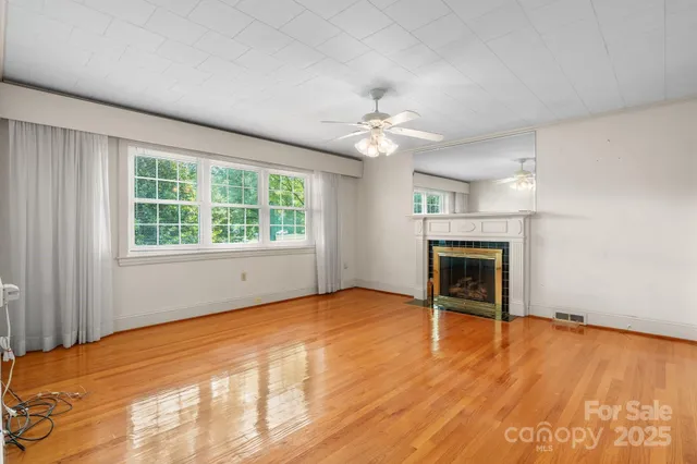 an empty room with wooden floor chandelier fan and windows