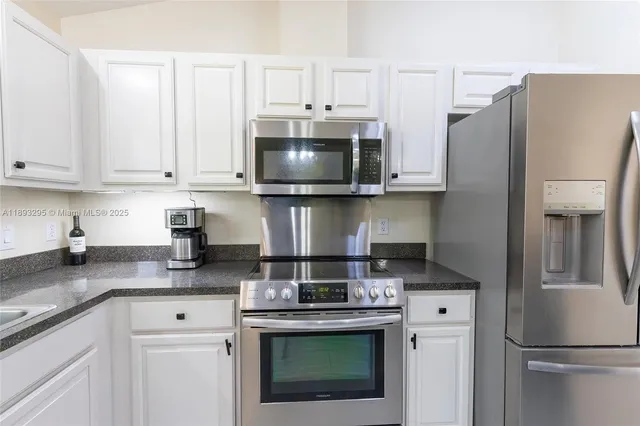 a kitchen with stainless steel appliances granite countertop a refrigerator a stove a sink and white cabinets