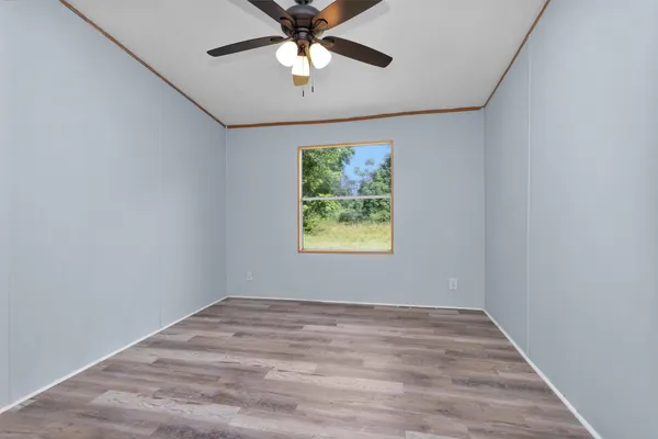 an empty room with wooden floor chandelier fan and windows