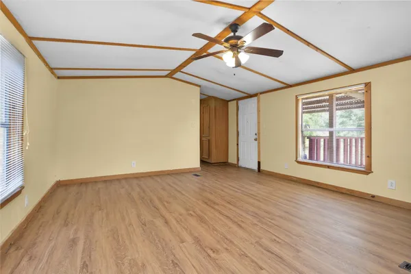 an empty room with wooden floor fan and windows