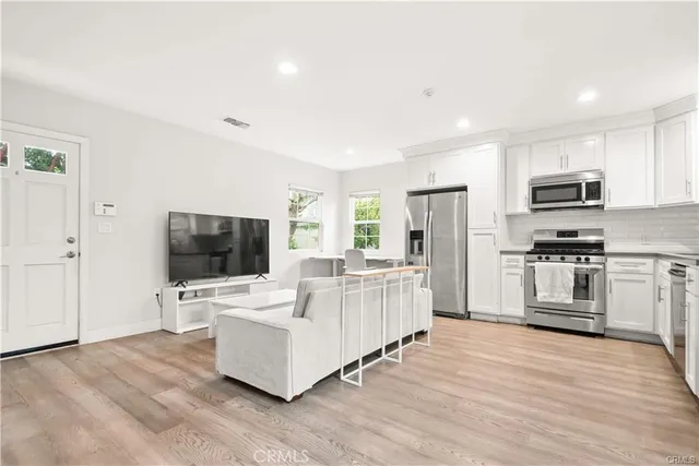 a kitchen with stainless steel appliances granite countertop white cabinets a sink a stove a microwave and wooden floors