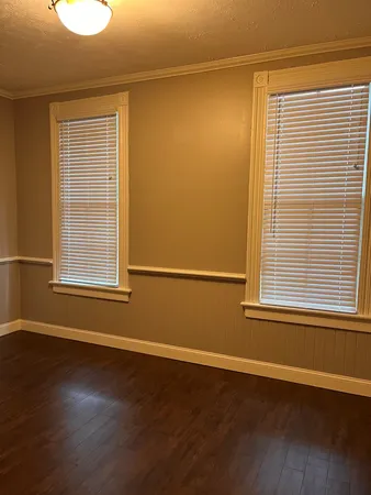 an empty room with wooden floor and windows with curtains