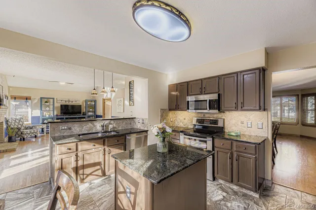 a kitchen with stainless steel appliances granite countertop a stove top oven a sink dishwasher a dining table and chairs with wooden floor