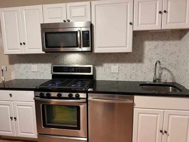 a kitchen with stainless steel appliances granite countertop white cabinets a stove top oven and granite counter tops