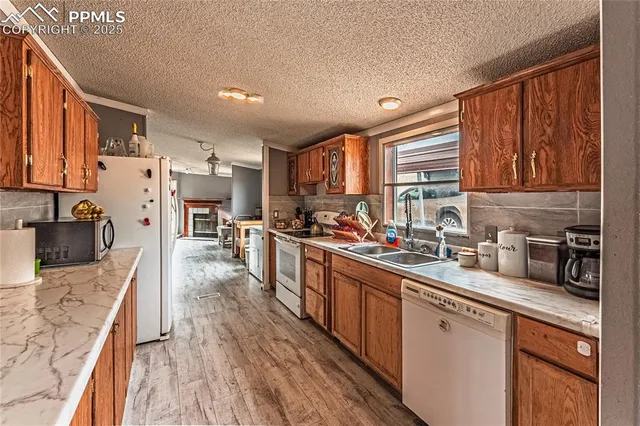 a kitchen with stainless steel appliances granite countertop wooden cabinets a refrigerator a sink a stove and a center island with wooden floor