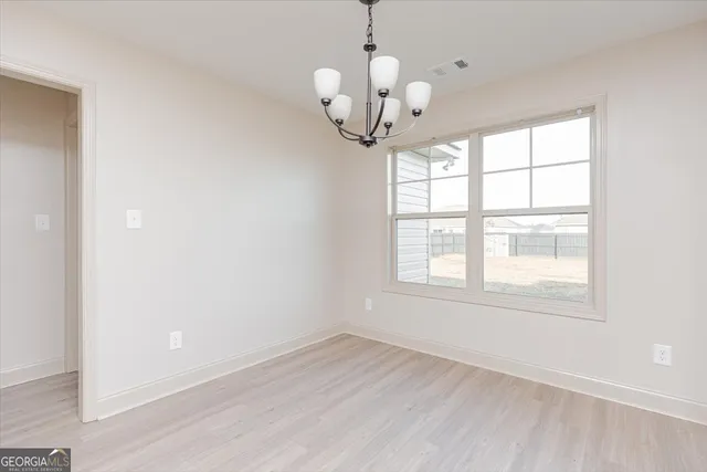 an empty room with wooden floor chandelier and window