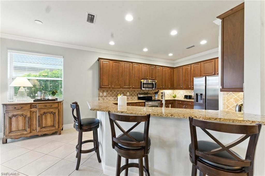 6899 Del Mar Terrace Naples, FL 34105 - Photo 17 of 41 a kitchen with stainless steel appliances kitchen island granite countertop a refrigerator a stove top oven a sink with a dining table and chairs with wooden floor