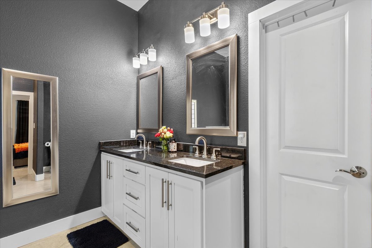 145 Cardinal Loop Paige, TX 78659 - Photo 27 of 40 A twin-sink vanity with dark granite countertops and white cabinetry offers practical appeal in this well-appointed bathroom.