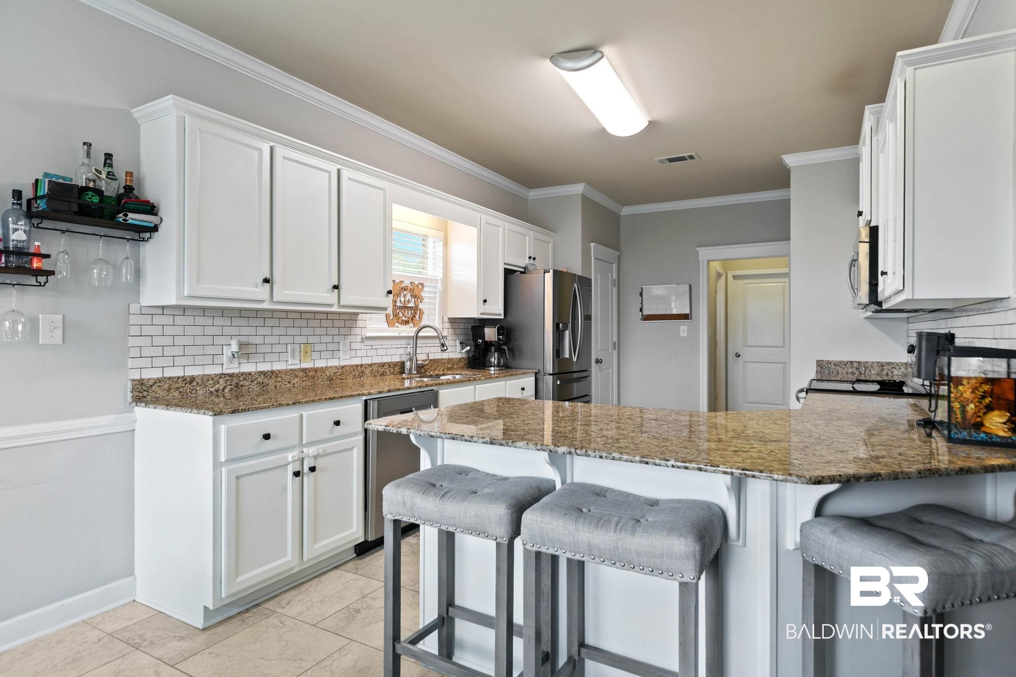 9177 Labrador Trail Theodore, AL 36582 - Photo 9 of 24 Kitchen featuring dark stone counters, a peninsula, white cabinets, and crown molding