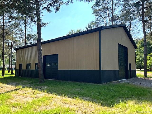 20285 29 Mile Road Ray, MI 48096 - Photo 23 of 25 Large metal-clad utility building with a two-tone exterior, featuring two overhead garage doors, multiple windows, and a side entry door, surrounded by mature trees