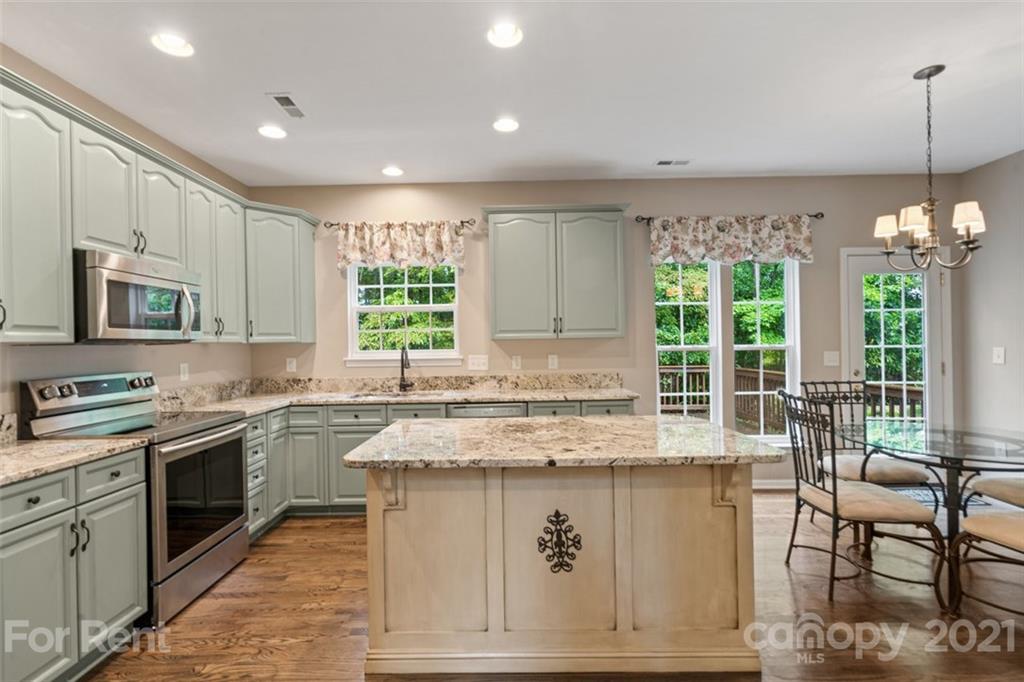 3028 Strawberry Road Matthews, NC 28104 - Photo 9 of 40 a kitchen with stainless steel appliances granite countertop a stove top oven a sink dishwasher a dining table and chairs with wooden floor