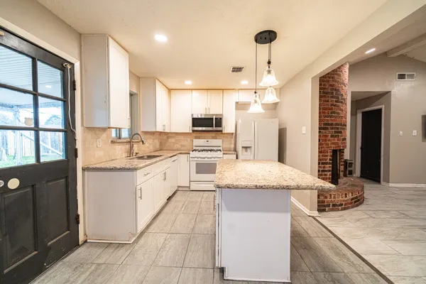 a large kitchen with granite countertop a large counter top a sink stainless steel appliances and cabinets