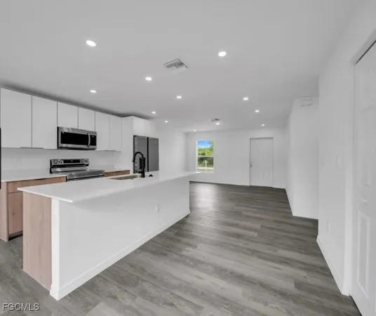 a view of kitchen with stainless steel appliances granite countertop a stove a sink a refrigerator and white cabinets with wooden floor