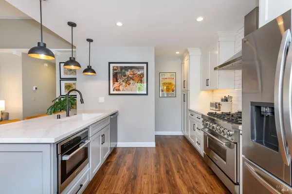 a kitchen with stainless steel appliances a stove top oven a sink a refrigerator and a wooden floor