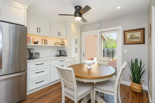 a kitchen with stainless steel appliances a dining table a stove a refrigerator and white cabinets with wooden floor