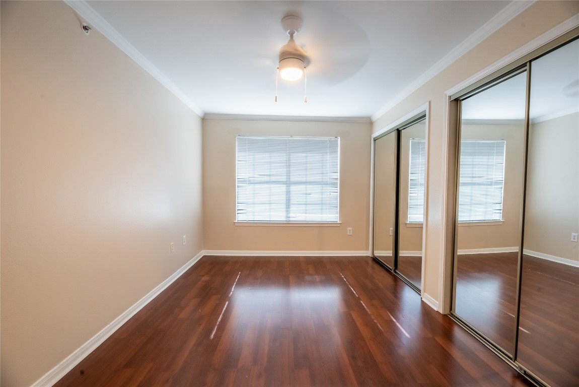 501 West 26th Street, Unit 323 Austin, TX 78705 - Photo 6 of 12 Unfurnished bedroom featuring two closets, dark wood-type flooring, ornamental molding, a ceiling fan, and multiple windows