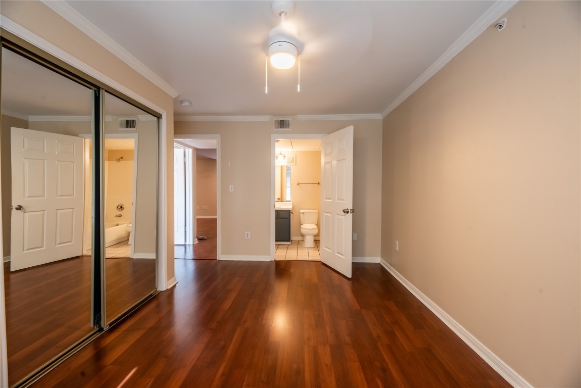 501 West 26th Street, Unit 323 Austin, TX 78705 - Photo 7 of 12 Unfurnished bedroom featuring a closet, dark wood-style floors, crown molding, ensuite bathroom, and ceiling fan