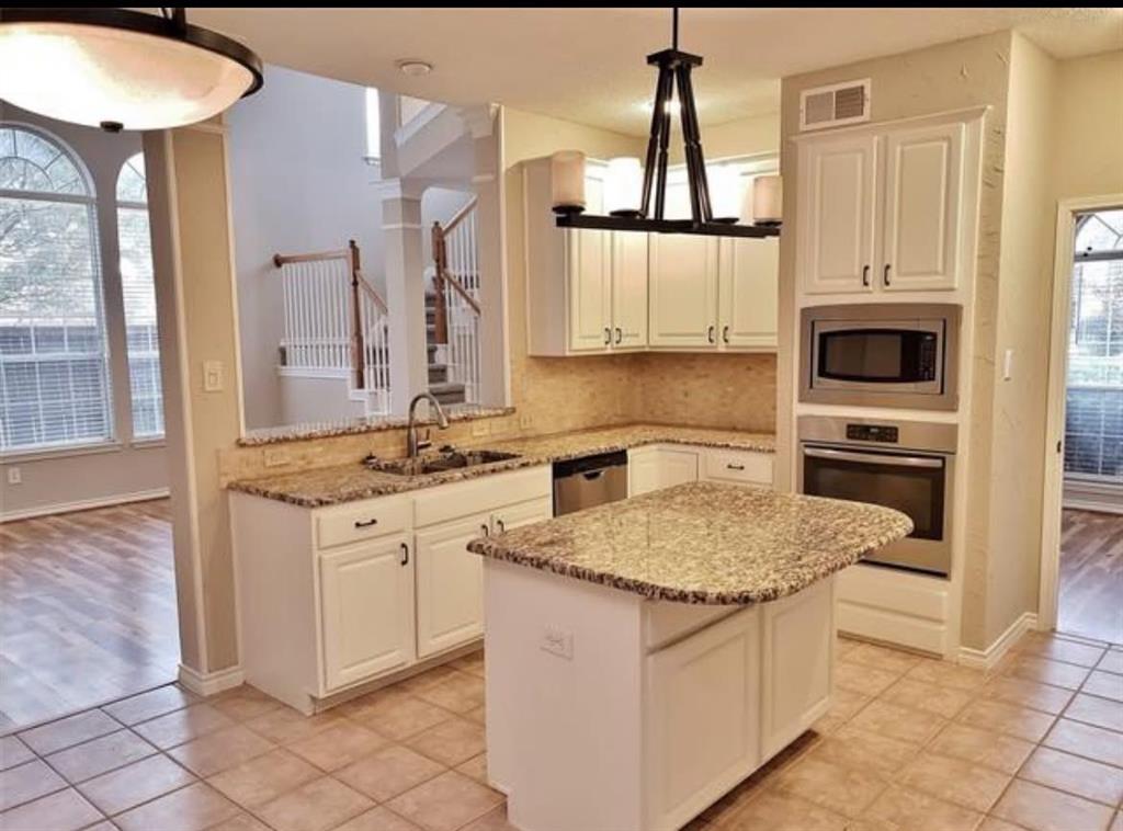 211 Moss Hill Road Irving, TX 75063 - Photo 7 of 14 Kitchen with stainless steel appliances, light stone countertops, a center island, and white cabinets