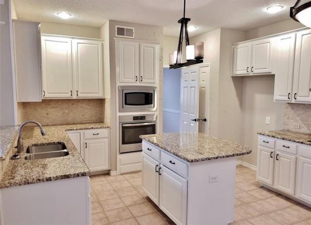 211 Moss Hill Road Irving, TX 75063 - Photo 8 of 14 Kitchen with tasteful backsplash, stainless steel appliances, white cabinets, light stone countertops, and a kitchen island
