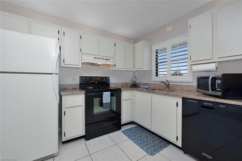 4258 27th Court Southwest, Unit 203 Naples, FL 34116 - Photo 4 of 15 Kitchen featuring a textured ceiling, light tile patterned flooring, sink, white cabinets, and black appliances