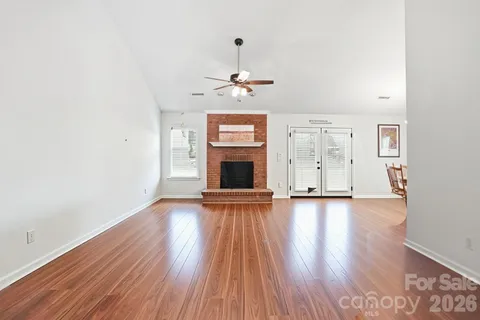 a view of an empty room with wooden floor fireplace and a window