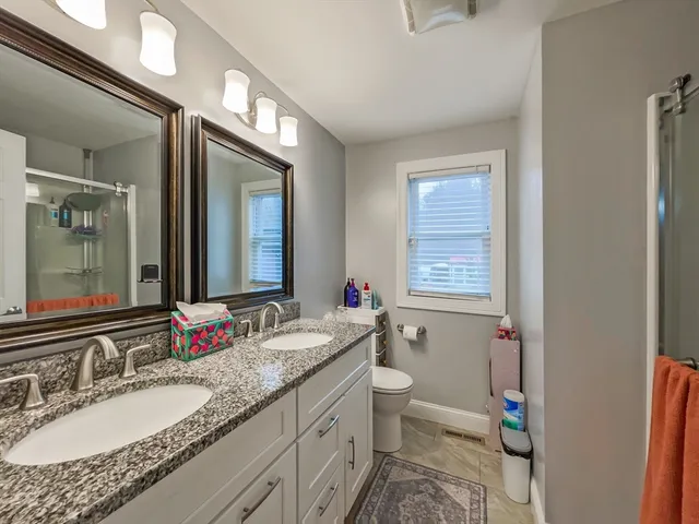 a bathroom with a granite countertop double vanity sink a mirror and a shower