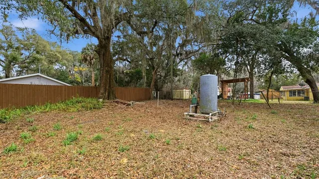 a backyard of a house with large trees and covered with wooden fence