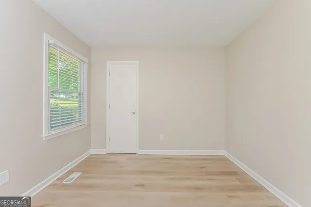 a view of an empty room with wooden floor and a window