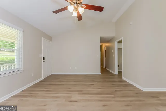 an empty room with wooden floor chandelier fan and windows