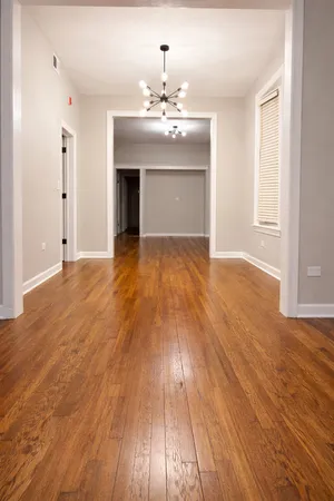 an empty room with wooden floor chandelier and windows
