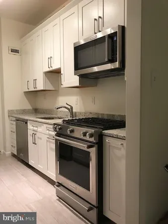 a kitchen with stainless steel appliances granite countertop white cabinets a microwave a sink and a counter