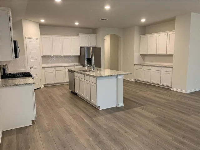 a kitchen with stainless steel appliances granite countertop a stove top oven a sink dishwasher and a refrigerator with wooden floor