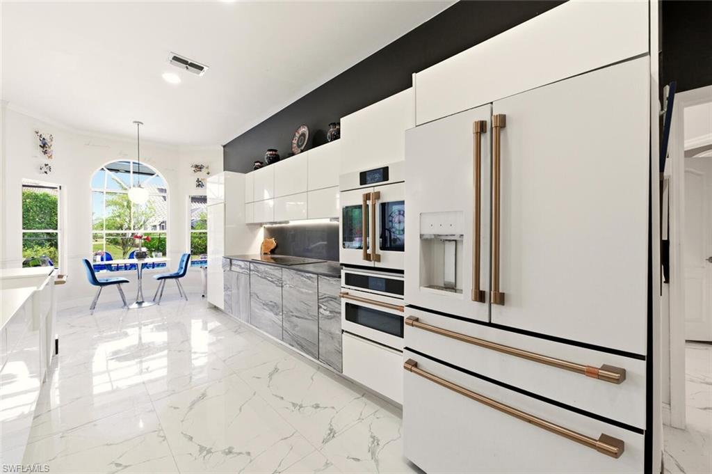 209 Countryside Drive Naples, FL 34104 - Photo 10 of 50 Kitchen featuring white appliances, decorative light fixtures, modern cabinets, light marble finish floors, and white cabinetry