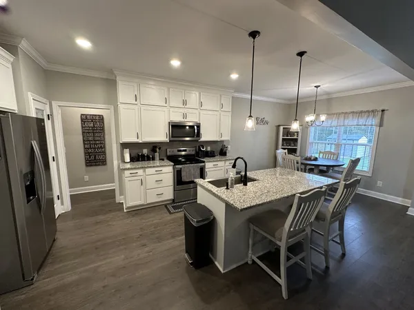 a kitchen with stainless steel appliances kitchen island granite countertop a refrigerator a stove a sink a dining table and chairs with wooden floor