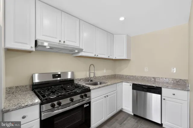 a white kitchen with granite top and stainless steel appliances